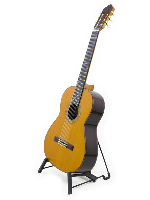 A 2021 Francisco Esteve 9C/B Classical guitar rests on a stand, contrasted against a simple white background, emphasizing its beauty.