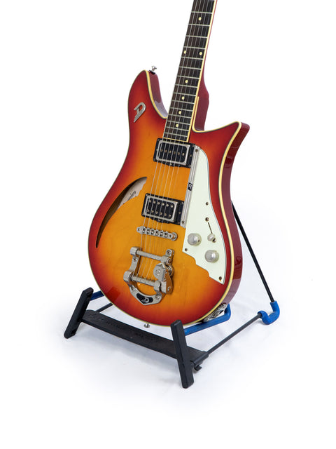 A Duesenberg Double Cat 6-string guitar displayed on a stand, featuring a striking white background that highlights its craftsmanship.
