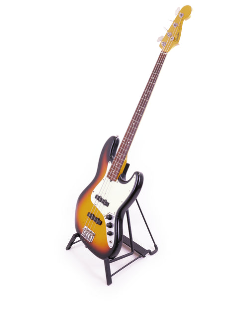 A Fender Custom Shop '64 Jazz Bass Relic on a stand, set against a clean white background, showcasing its vintage design.