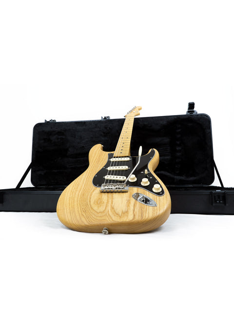 A Fender Limited Edition Stratocaster guitar in a case, featuring a natural oiled ash design, set on a white backdrop.