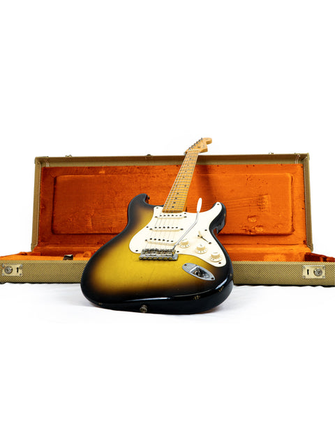 A Fender guitar, specifically a Time Machine 58 Strat Relic from 2008, rests in a vibrant orange case, emphasizing its retro appeal.
