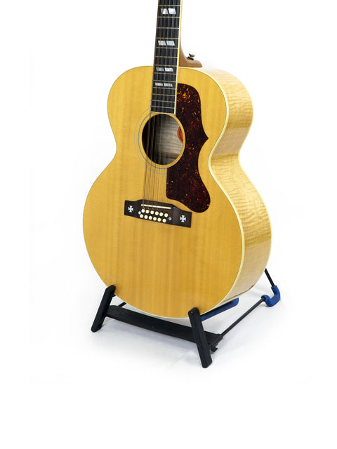 A Gibson J-185-12 string guitar displayed on a stand, set against a bright white background, highlighting its craftsmanship.