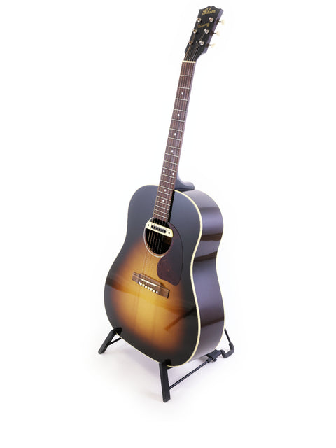A Gibson J-45 True Vintage acoustic guitar displayed on a stand with a white backdrop, highlighting its craftsmanship.