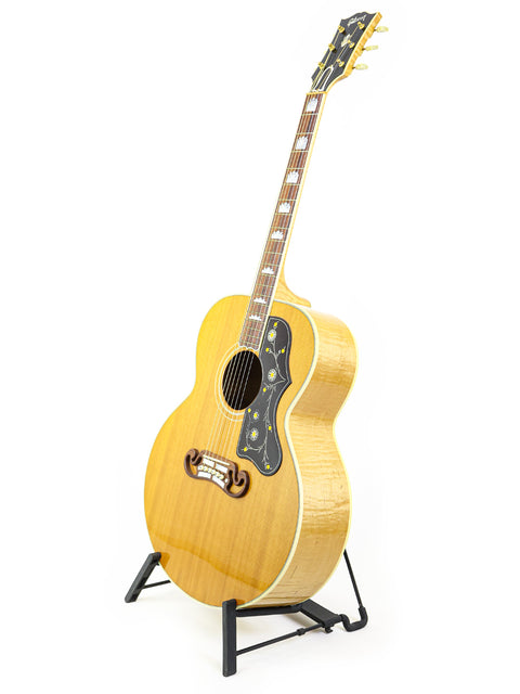 A Gibson SJ-200 guitar from 2001 displayed on a stand against a clean white background.