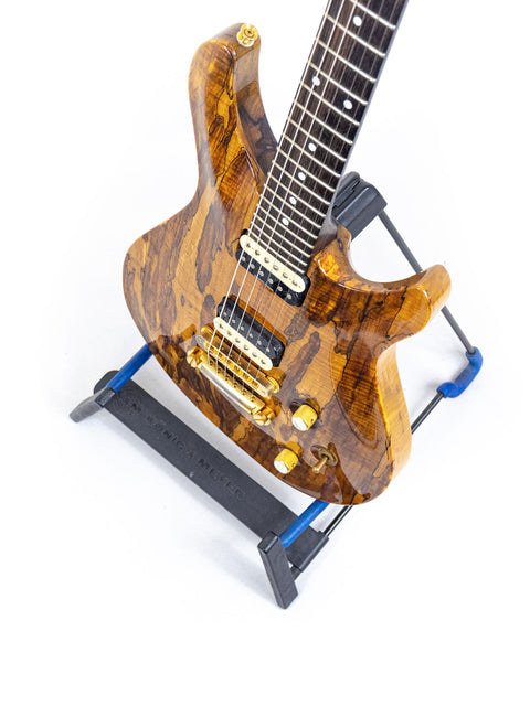 A PRS-style Ed Roman Quicksilver guitar with a wooden body elegantly resting on a stand, made in the USA, 2004.