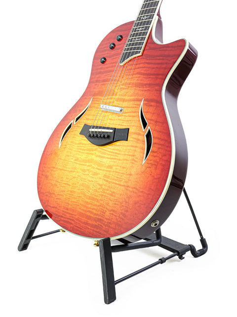 A Taylor T5-C1 guitar displayed on a stand, with a striking red backdrop highlighting its craftsmanship.