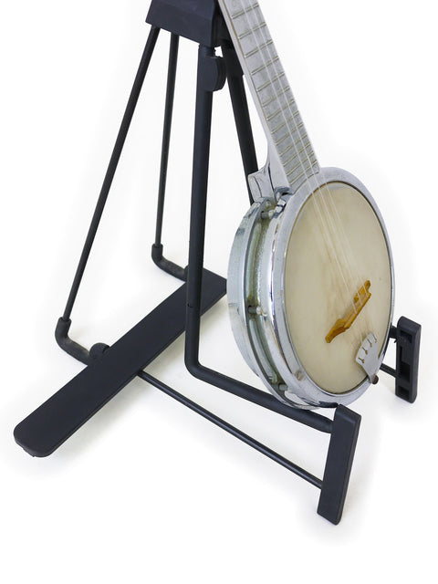 A banjo resting on a black guitar stand against a white background.