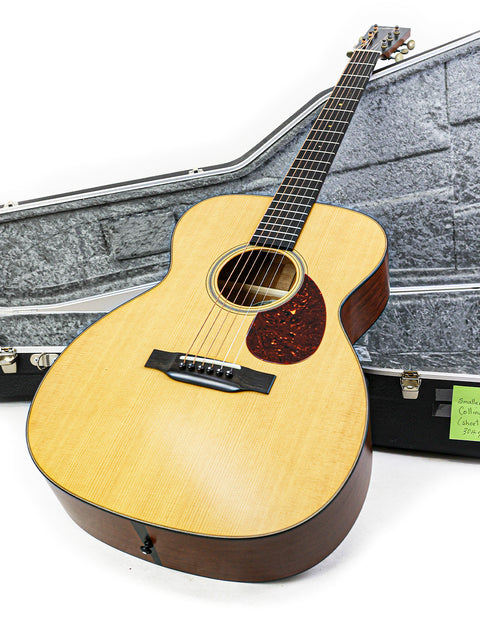 A beautiful Collings Julian Lage Signature OM1 guitar lies in its case, paired with a guitar strap, reflecting artistry and attention to detail.