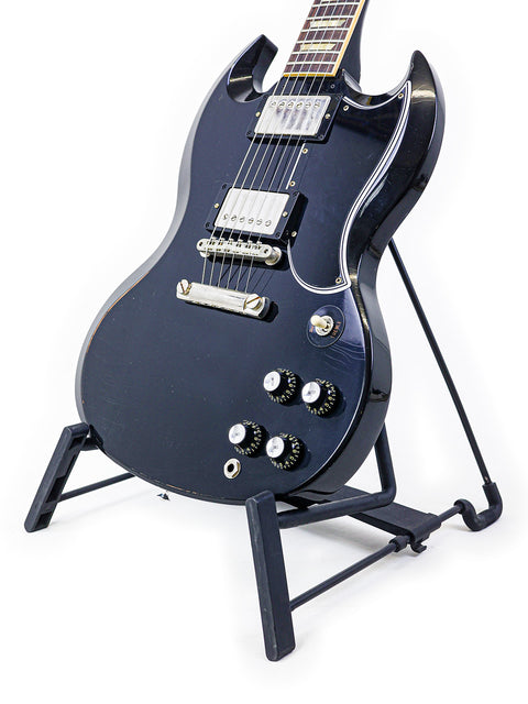 A black '64 SG guitar from Gibson's Custom Shop on a stand, set against a bright white background.
