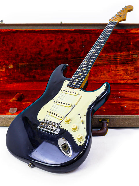 A black Fender L-Series Stratocaster guitar from 1963, elegantly resting in a wooden case, highlighting its classic style.