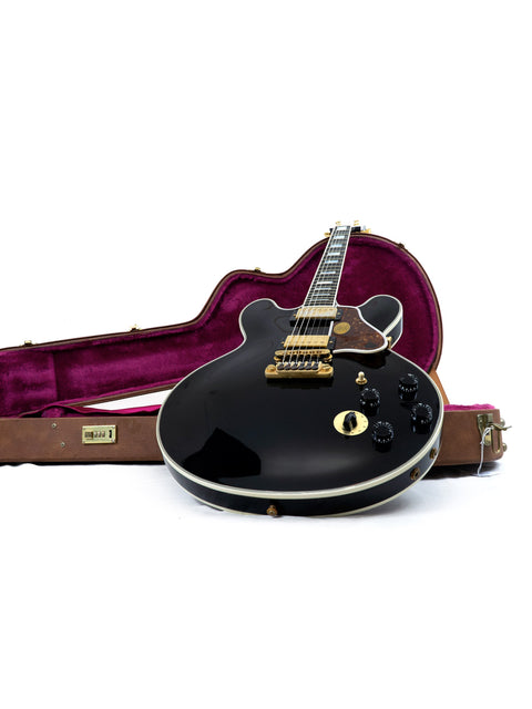 A black Gibson Lucille guitar with a protective case, showcasing signatures from BB King and Eric Clapton, on a white surface.