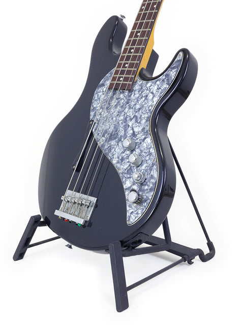 A black bass guitar, Line 6 Variax from Korea 2004, elegantly positioned on a stand with a simple white background.