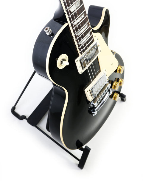 A black electric guitar, a 1995 Gibson Les Paul Standard, elegantly positioned on a stand, highlighting its classic features.