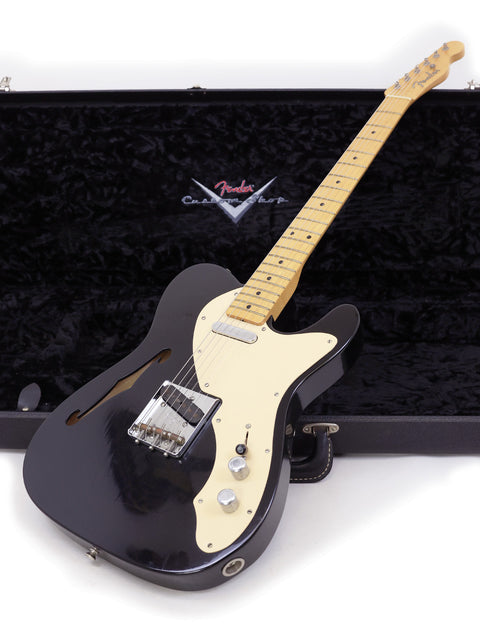 A black electric guitar, a 2005 Fender Custom Shop Telecaster Thinline, securely housed in a case.