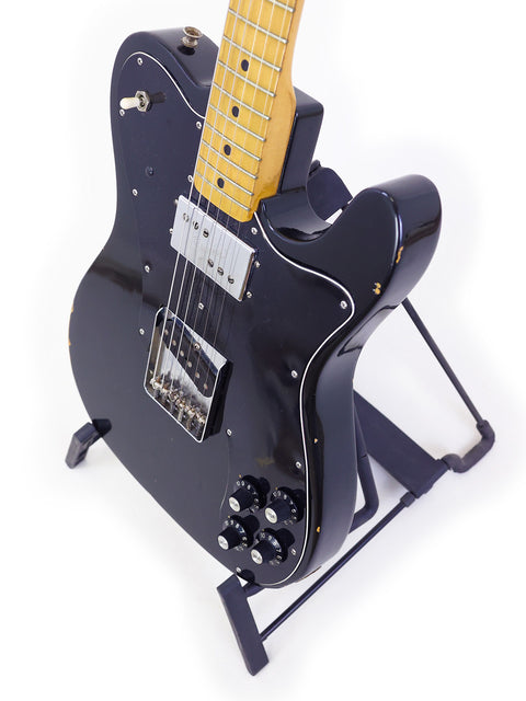 A black electric guitar, the 1978 Fender Telecaster Custom, showcased on a stand, illustrating its timeless craftsmanship.