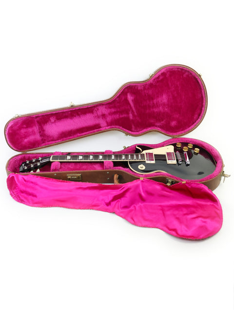 A black guitar case featuring pink lining contains a pink Gibson Les Paul Standard guitar, model year 1995, in a vibrant display.