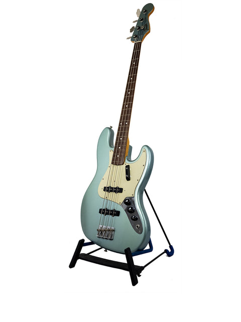 A blue electric bass guitar on a black stand against a white background.