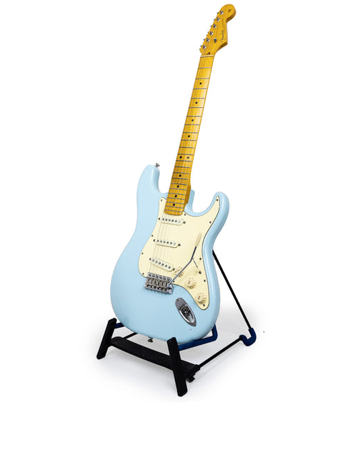 A blue electric guitar on a stand, showcasing its sleek design against a clean white background. Warmoth Strat Partscaster, USA 2012.