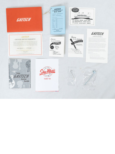 A box filled with a Gretsch G6131 Malcolm Young Signature Jet guitar, guitar picks, and assorted music accessories.