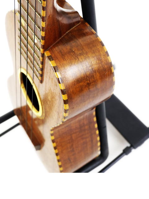 A classic 1924 Weissenborn Miami Style 3 Koa Ukulele resting on a stand, showcasing its timeless beauty.
