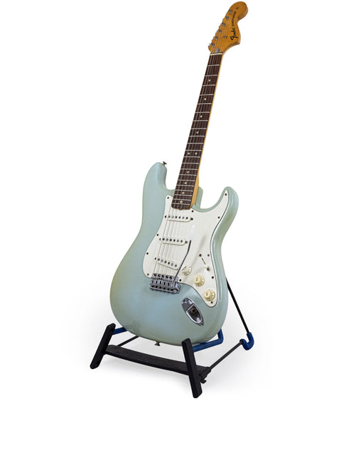 A classic 1972 Fender Stratocaster guitar displayed on a stand, set against a white backdrop, labeled as sold.