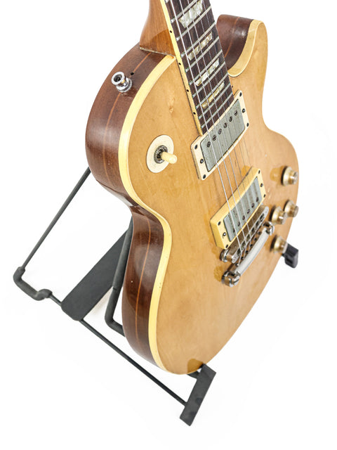 A classic 1973 Gibson Les Paul Deluxe guitar on a stand, set against a bright white background.