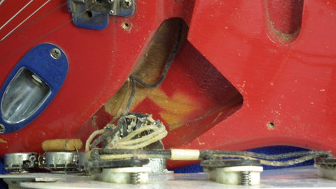 A close-up of a 1957 Fender Stratocaster, Dakota Red, displaying its internal wires and mechanical parts.

