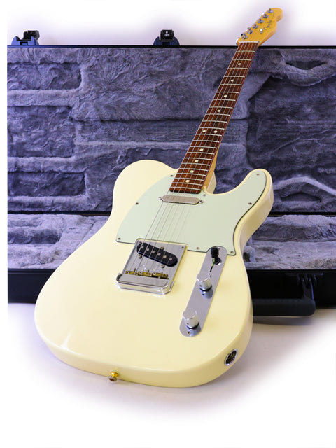 A cream-colored electric guitar leaning against a stone-textured wall.