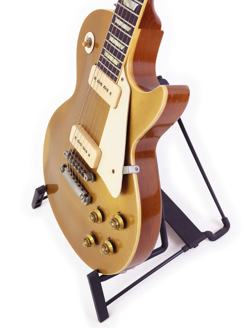 A gold 1956 Reissue Gibson Les Paul guitar on a stand, with a white background emphasizing its luxurious finish and craftsmanship.