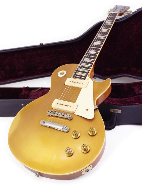 A gold guitar, a Gibson Les Paul 1956 reissue, lies in its case on the floor, highlighting its classic design and modern upgrades.