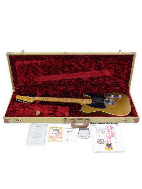 A golden electric guitar in a red velvet-lined case with documents and a book beside it.