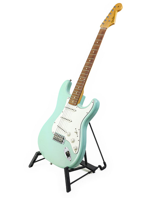A green guitar, the 1960's Closet Classic Stratocaster, stands elegantly on a stand with a white background.