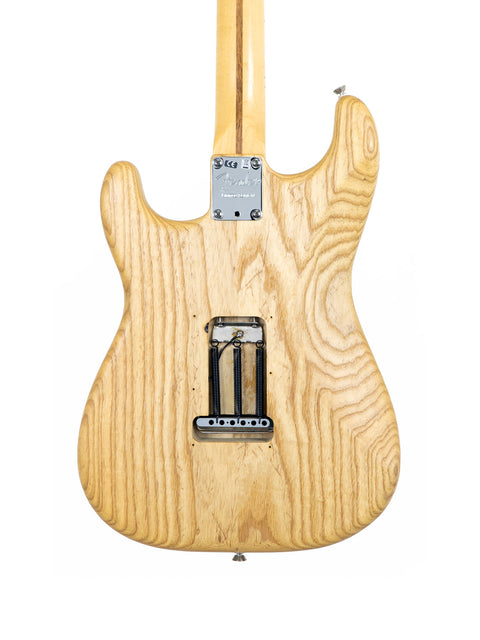 A natural oiled ash Fender Stratocaster guitar, emphasizing its wooden body and neck, perfect for music enthusiasts.