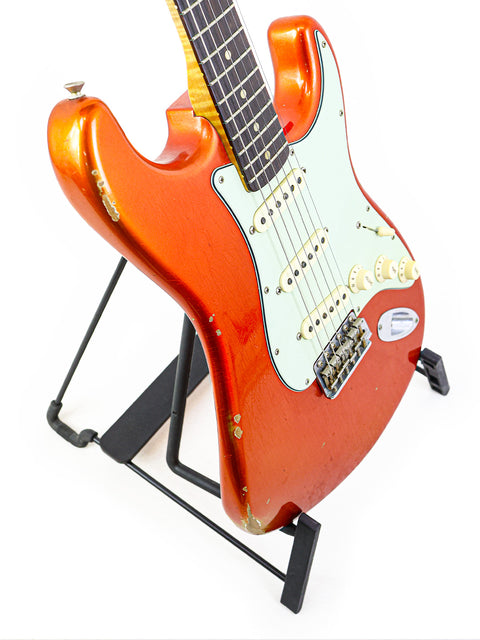A red-bodied Fender Ltd NAMM '64 Stratocaster Relic guitar elegantly positioned on a stand, highlighting its classic appeal.