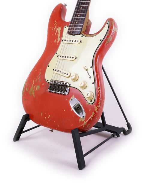 A red 1964 Fender L Series Stratocaster guitar on a stand, set against a clean white backdrop.