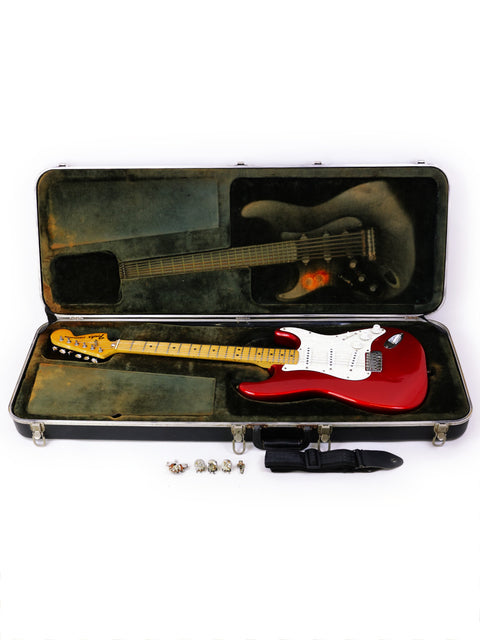 A red 1979 Fender Stratocaster guitar nestled in a case, with two guitar picks resting beside it, highlighting its classic design.