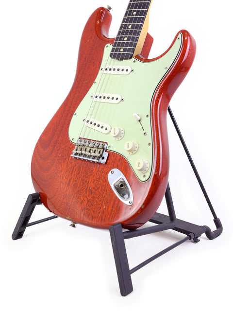 A red 2019 Fender Custom Shop Stratocaster guitar elegantly positioned on a stand, set against a bright white background.