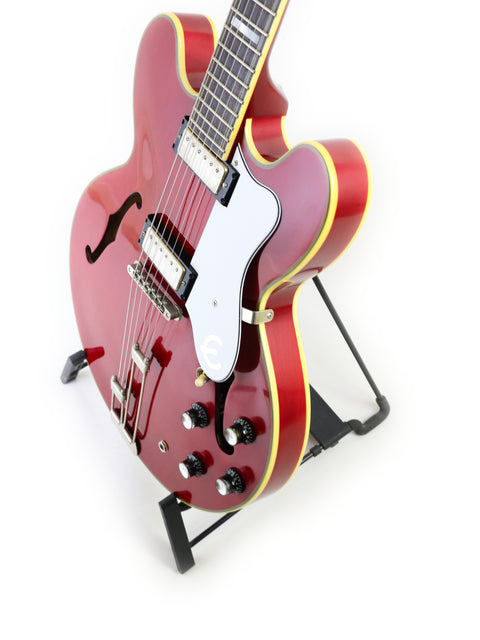 A red Epiphone 50th Anniversary 1962 Sheraton E212T Reissue guitar rests elegantly on a stand, showcasing its vibrant color.
