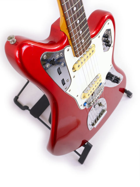 A red Fender CIJ Jaguar electric guitar, made in Japan (1999-2002), resting on a stand, highlighting its sleek design.