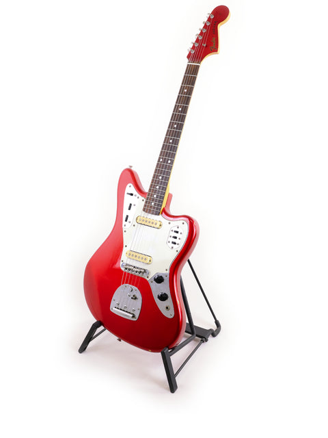 A red Fender CIJ Jaguar guitar elegantly positioned on a stand, contrasted by a bright white background for visual impact.