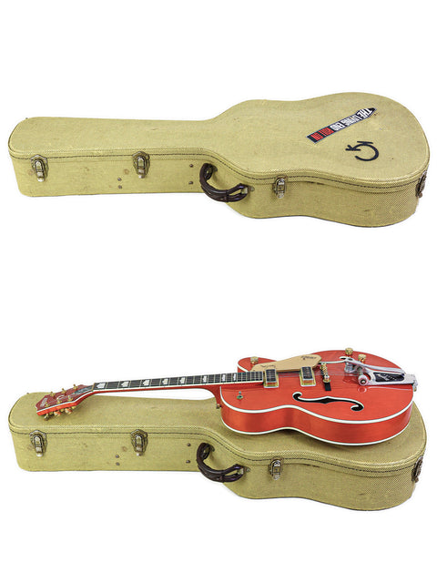 A red Gretsch 6120DE Duane Eddy Signature guitar rests atop two guitars in a case, highlighting its striking design.