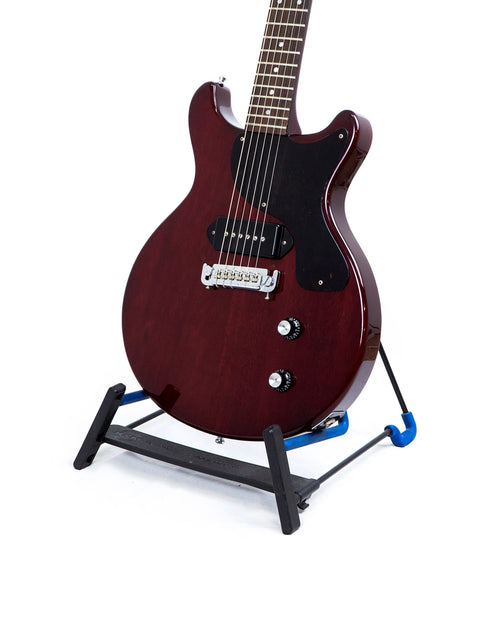 A red electric guitar, the Burny Les Paul Jr from the 1980s, positioned on a blue stand, perfect for rock enthusiasts.