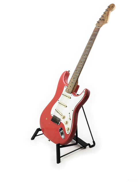 A red vintage Fender Stratocaster guitar from 1958, showcased on a stand with a smooth white background, capturing its timeless elegance.