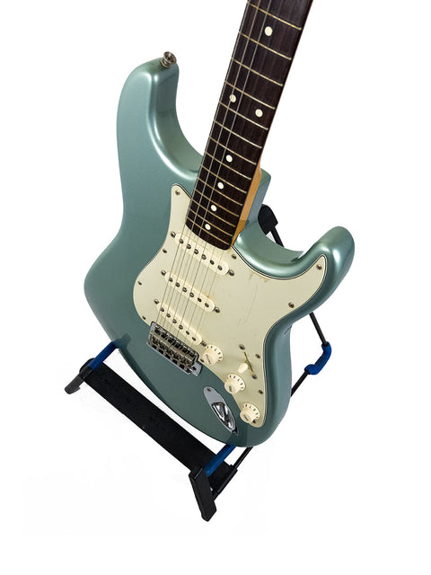 A seafoam green electric guitar on a black stand with a white background.