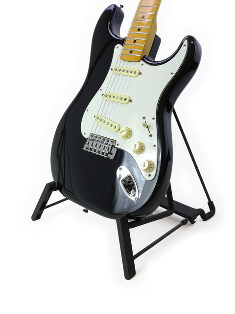 A sleek black 1981 Fender Stratocaster guitar on a stand, highlighted by a crisp white background for a timeless appeal.