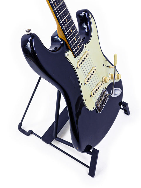 A sleek black Fender L-Series Stratocaster guitar displayed on a stand, set against a bright white backdrop.
