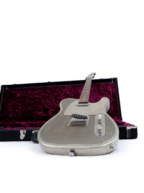 A sleek silver guitar, the James Trussart Holey Nickel Steelcaster, displayed in its case on a bright white backdrop.
