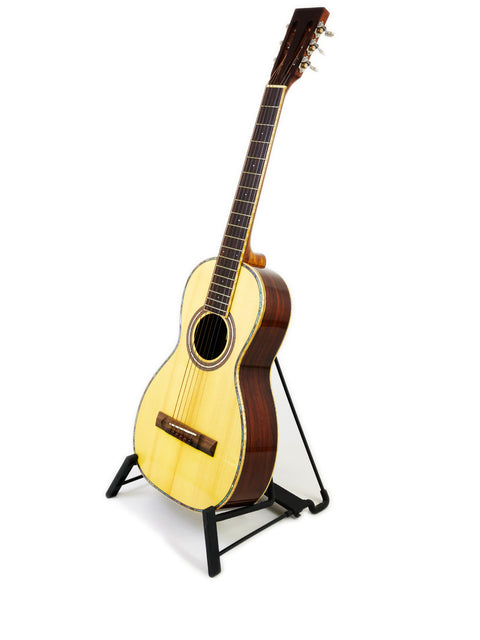 A small guitar displayed on a stand with a clean white background, highlighting its features. Gilet Bay State, Australia 2018.