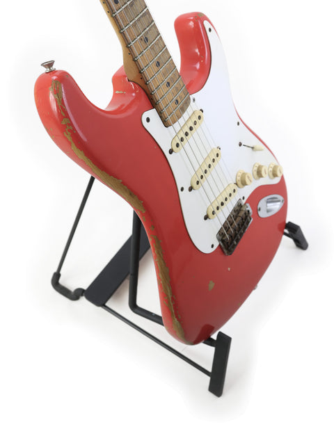 A striking red 1958 Fender Stratocaster guitar on a stand, set against a minimalist white backdrop.