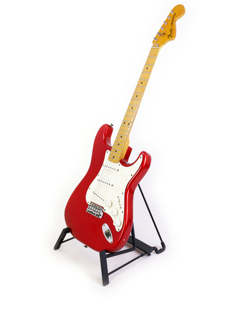 A striking red Fender Stratocaster guitar from 1979 displayed on a stand, with a minimalist white backdrop.
